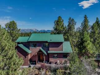 Experience serene mountain living in this stunning wood-sided home, featuring a durable green metal roof and nestled amidst towering pine trees.