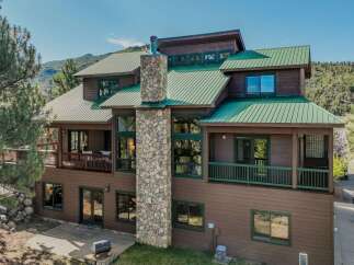 Experience mountain living in this stunning home featuring a durable green metal roof and a striking stone chimney.