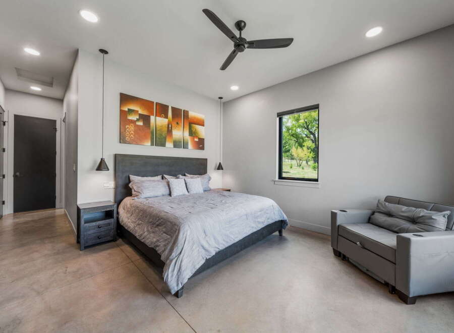 This modern bedroom boasts a sleek design with a comfortable bed, stylish artwork, and a ceiling fan.