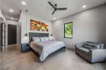 This modern bedroom boasts a sleek design with a comfortable bed, stylish artwork, and a ceiling fan.