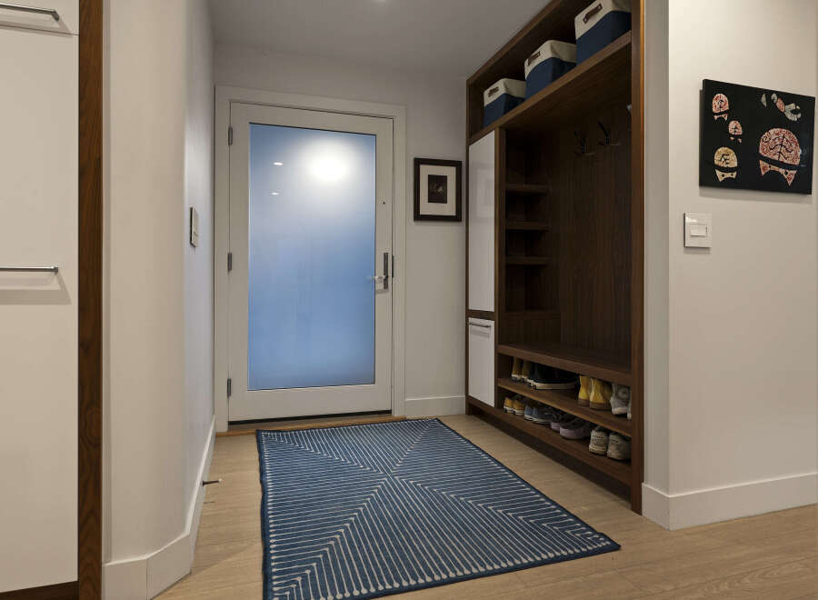 Step into this inviting entryway, showcasing a modern design with a built-in storage unit and a stylish blue rug.