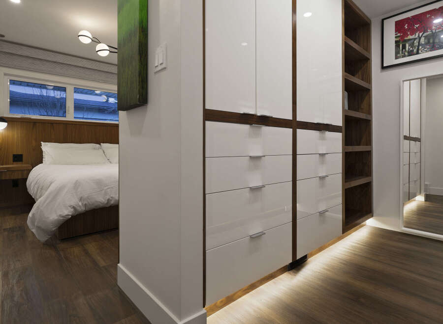 This stunning bedroom boasts a modern design with sleek, white cabinetry and rich, dark wood flooring.