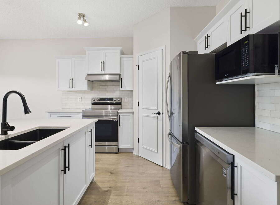Step into this stunning kitchen, boasting modern white cabinetry and sleek black hardware.