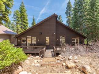 Nestled amidst towering trees, this stunning property boasts a dark wood exterior and a welcoming deck.