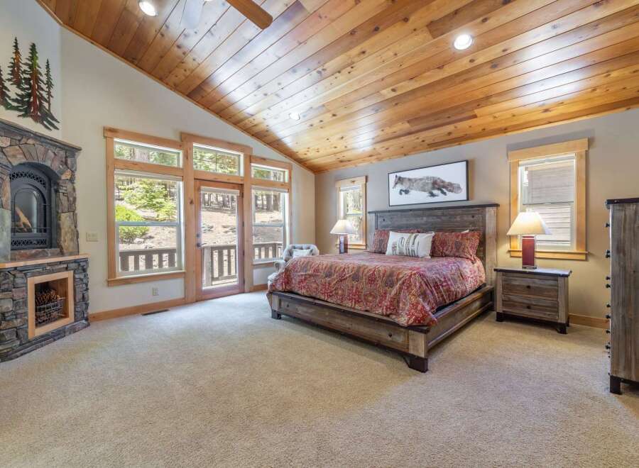 Step into luxury with this stunning bedroom featuring a cozy fireplace and a rustic wooden ceiling.