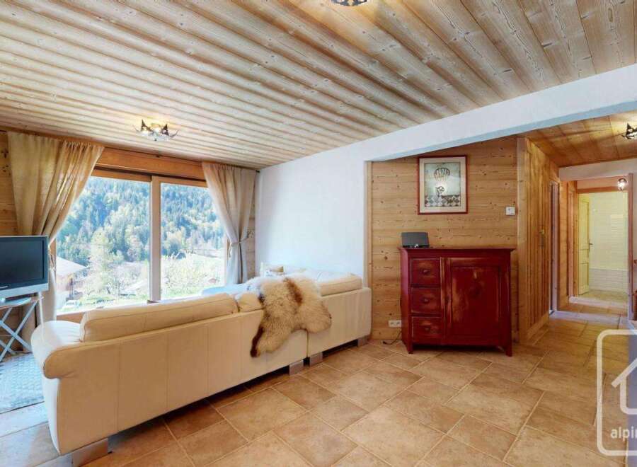 Discover the charm of this stunning property, featuring a cozy living room with a beautiful wooden ceiling and large windows that offer breathtaking views of the surrounding mountains.