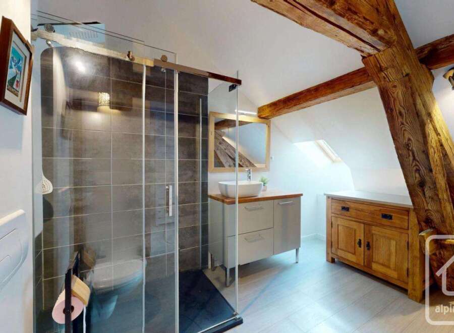 Discover this stunning bathroom featuring a modern glass shower, elegant vanity, and a touch of rustic charm with exposed wooden beams.