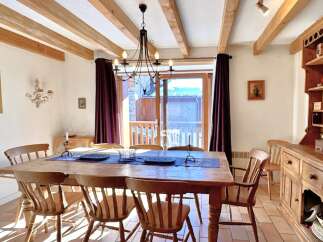 This charming dining room boasts a rustic aesthetic with exposed wooden beams and a large wooden dining table.