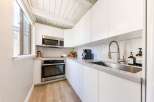 This modern kitchen boasts sleek white cabinetry, stainless steel appliances, and a stylish herringbone backsplash.