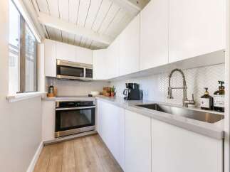 This modern kitchen boasts sleek white cabinetry, stainless steel appliances, and a stylish herringbone backsplash.