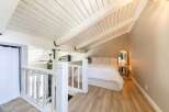 This charming loft bedroom features a bright and airy design with a vaulted, white-painted ceiling and exposed beams, creating a spacious feel.