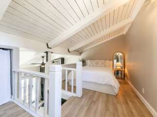 This charming loft bedroom features a bright and airy design with a vaulted, white-painted ceiling and exposed beams, creating a spacious feel.