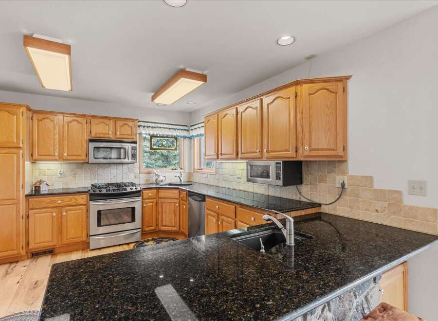 This stunning kitchen boasts beautiful wooden cabinetry and sleek black countertops, creating a warm and inviting atmosphere.