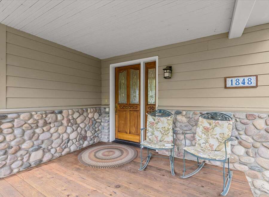 Welcome to this charming home! This property features a beautiful wooden door, inviting rocking chairs, and a cozy rug, perfect for relaxing.