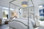 Step into a serene bedroom retreat, where natural light floods through expansive windows, illuminating the elegant four-poster bed.