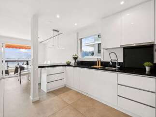 This stunning kitchen boasts sleek, modern design with pristine white cabinetry and a contrasting black countertop.