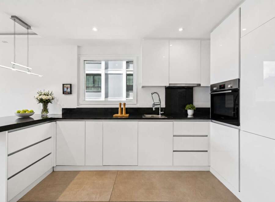 This modern kitchen boasts sleek, white cabinetry and a contrasting black countertop, creating a stylish and functional space.