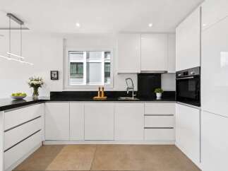 This modern kitchen boasts sleek, white cabinetry and a contrasting black countertop, creating a stylish and functional space.