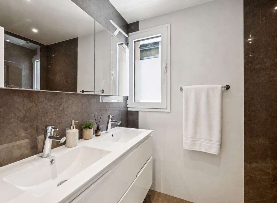 Step into a modern bathroom oasis! This stylish space features a sleek white vanity with dual sinks, complemented by a large mirror and elegant lighting.