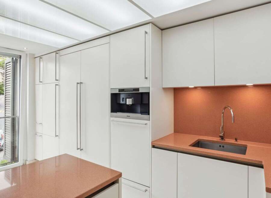 This modern kitchen boasts sleek, white cabinetry and a built-in coffee machine, perfect for the discerning homeowner.