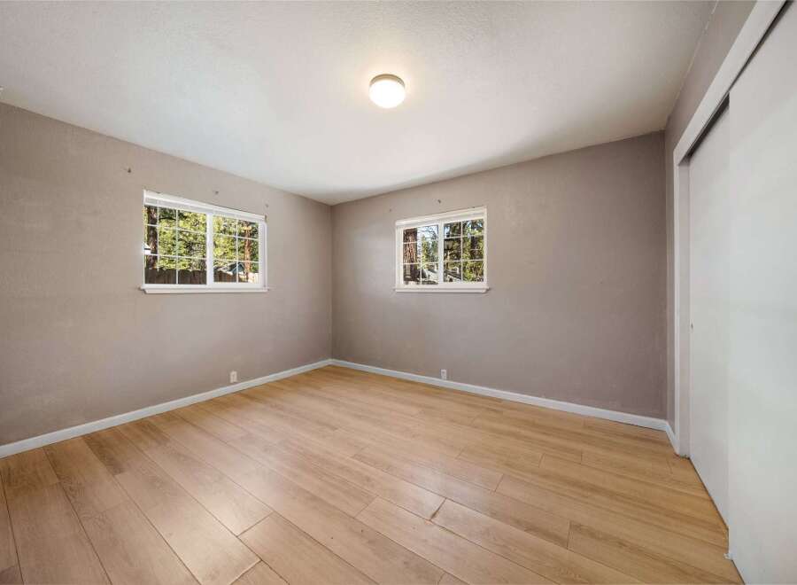 Step into this inviting bedroom, featuring natural light streaming through two windows, offering a serene view.