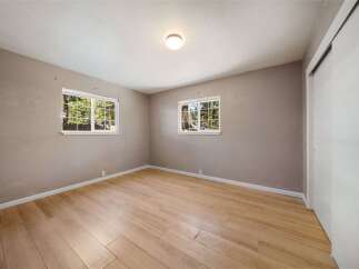Step into this inviting bedroom, featuring natural light streaming through two windows, offering a serene view.