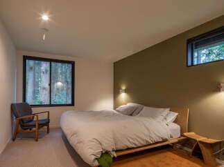 Experience tranquility in this modern bedroom, featuring a serene forest view through expansive windows.