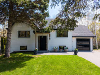 This stunning modern home boasts a sleek design with a bright white exterior and a dark, contrasting garage door.