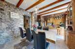 Step into rustic elegance with this stunning property, featuring a dining area with a stone wall and a wooden table.