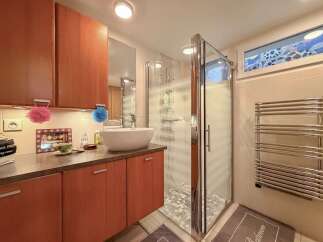 This modern bathroom features a sleek glass shower, a stylish vessel sink, and ample storage with wooden cabinets.