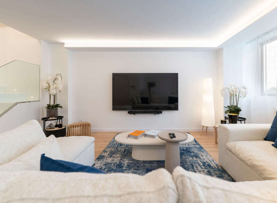 Experience modern living in this stunning property, featuring a spacious living room with a sleek, wall-mounted TV.