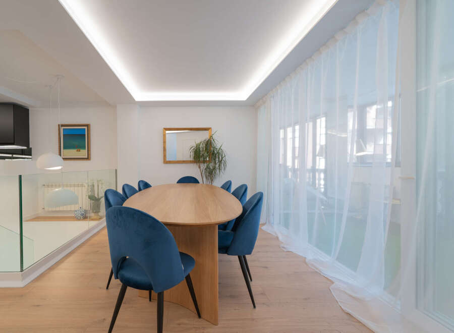 This stunning dining room features a modern design with an oval wooden table and plush blue velvet chairs, creating an inviting space for gatherings.