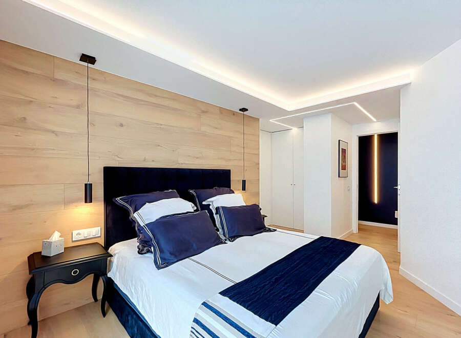 Experience modern luxury in this master bedroom, featuring a stunning wood-paneled accent wall and sleek, integrated LED lighting.