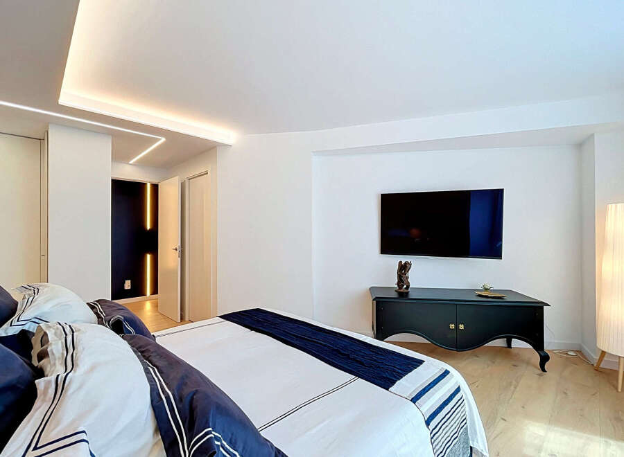 Experience modern luxury in this beautifully appointed bedroom, featuring a sleek mounted television and ambient LED ceiling lighting.