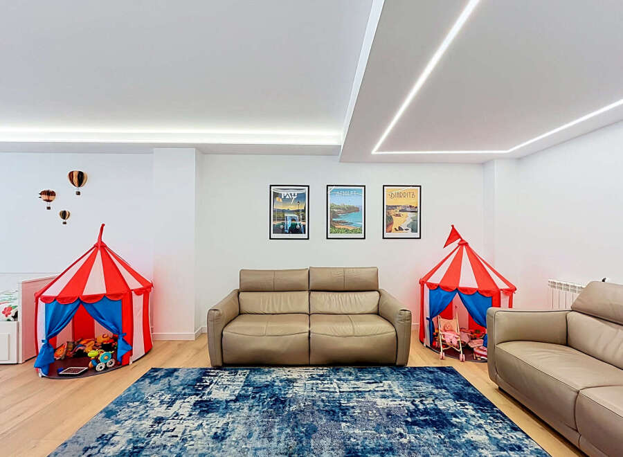 This spacious living area is perfect for families, featuring two comfortable leather sofas and a vibrant blue abstract rug.
