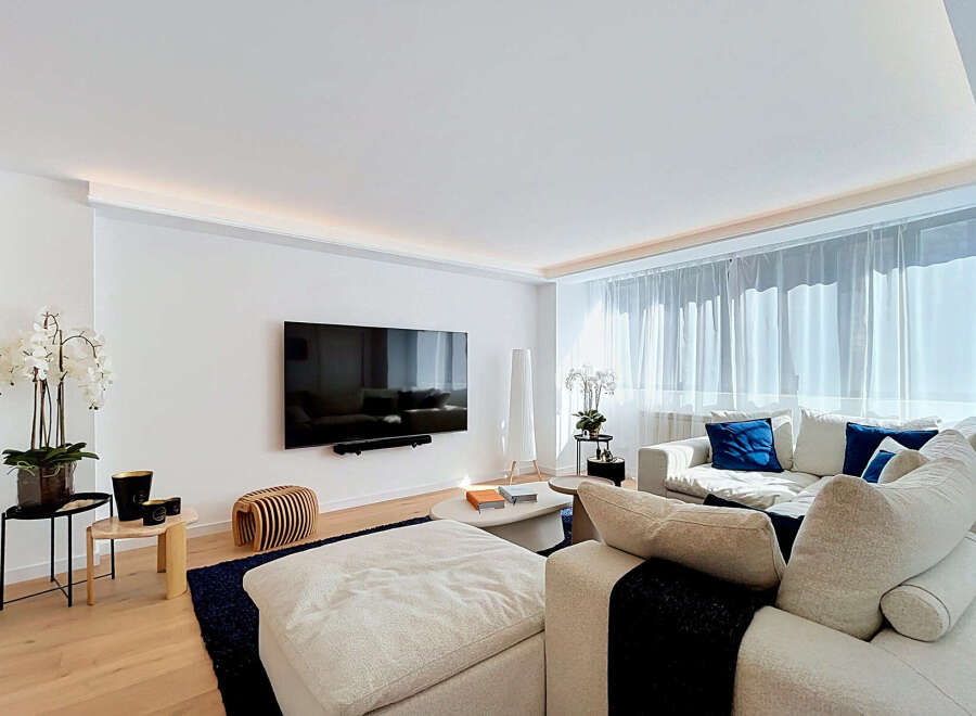 Experience modern luxury in this spacious living room, featuring a sleek wall-mounted TV and ambient recessed lighting.