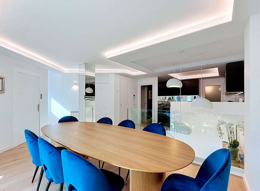 Experience modern luxury in this stunning dining area, featuring a sleek, oval-shaped wooden table complemented by vibrant blue velvet chairs.