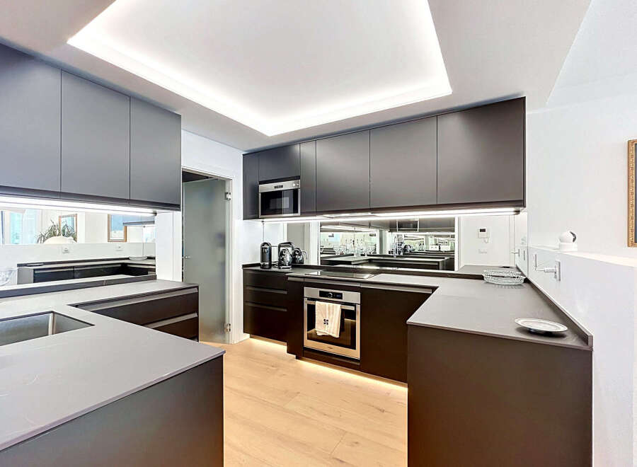 Experience modern luxury in this sleek, contemporary kitchen featuring dark cabinetry, integrated appliances, and a striking mirrored backsplash that amplifies the space.