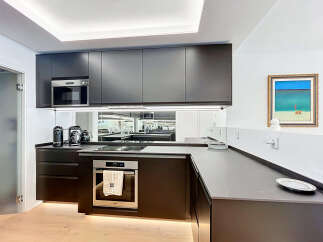 Experience modern luxury in this sleek kitchen, featuring dark cabinetry, integrated appliances including a microwave and oven, and a stylish induction cooktop.