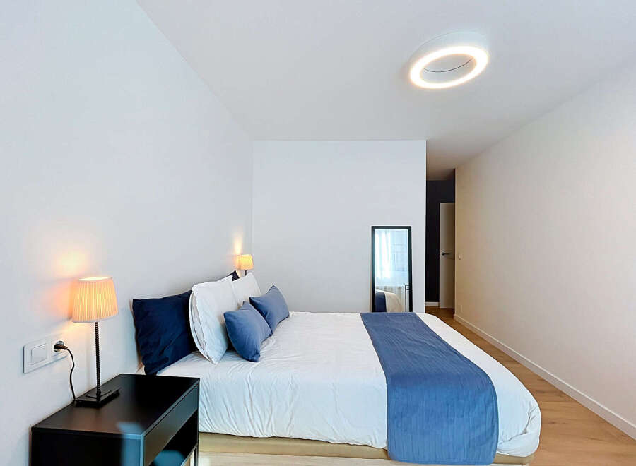 Experience modern comfort in this beautifully appointed bedroom, featuring a plush king-sized bed adorned with crisp white linens and elegant blue accent pillows.