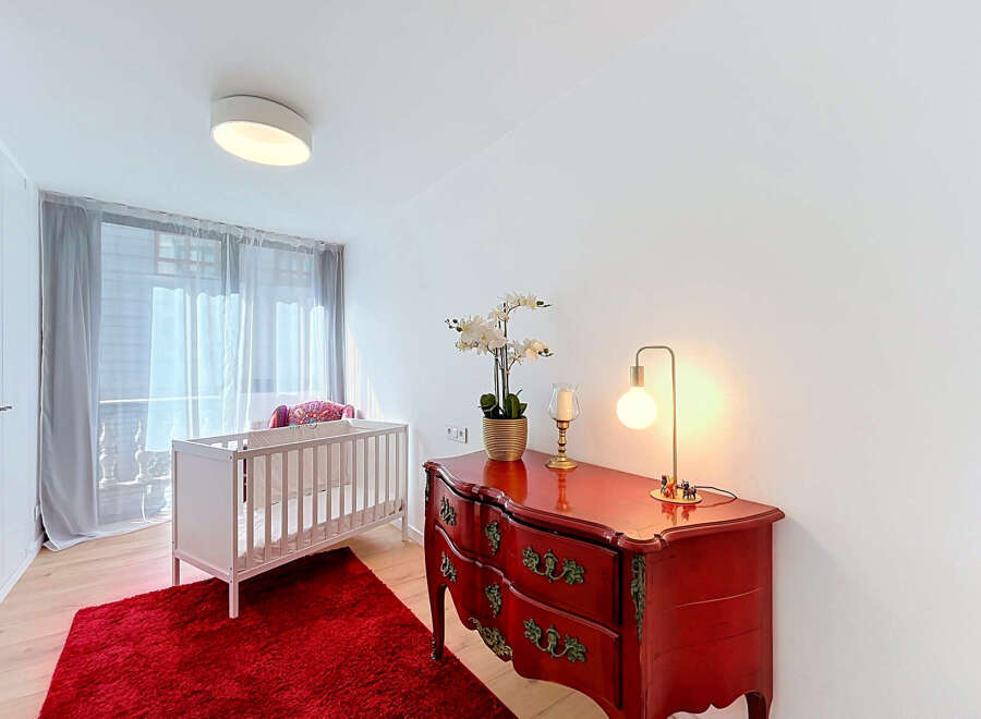 This charming nursery features a cozy white crib set against a vibrant red rug, creating a playful and inviting atmosphere.