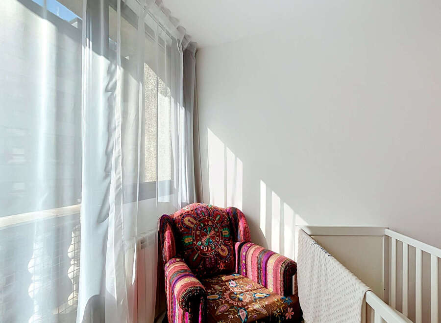 Bright and airy, this cozy corner features a vibrantly patterned armchair bathed in natural light streaming through sheer curtains.