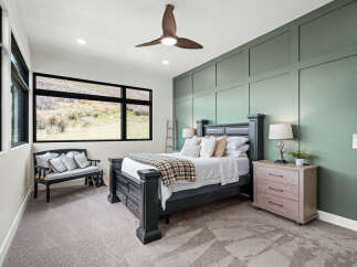 Step into luxury with this stunning bedroom, featuring a serene green accent wall and a stylish ceiling fan.