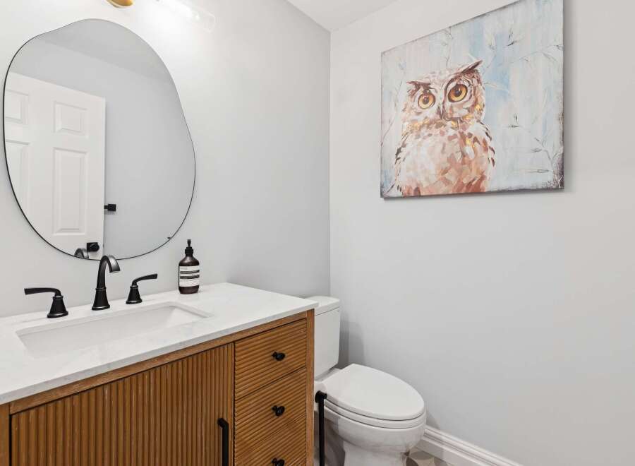 This stunning powder room showcases a modern design with a unique, textured wooden vanity and a sleek, oval mirror.