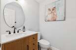 This stunning powder room showcases a modern design with a unique, textured wooden vanity and a sleek, oval mirror.