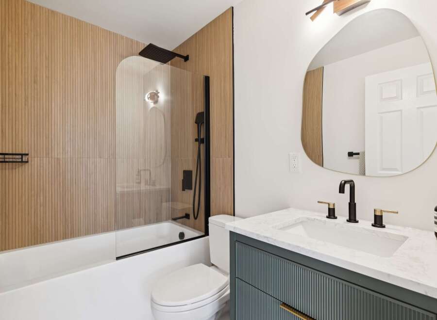 Step into a modern bathroom oasis! This stunning space features a sleek black shower system, a stylish vanity with a marble countertop, and a unique wood-paneled accent wall.