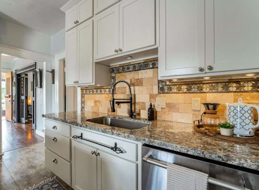 This stunning kitchen boasts elegant white cabinetry, a sleek stainless steel sink, and a beautiful granite countertop, creating a perfect blend of style and functionality.