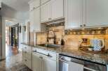 This stunning kitchen boasts elegant white cabinetry, a sleek stainless steel sink, and a beautiful granite countertop, creating a perfect blend of style and functionality.