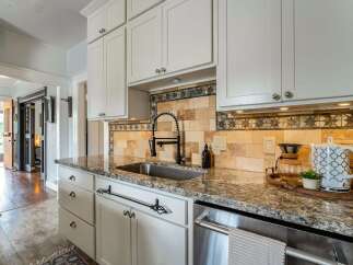 This stunning kitchen boasts elegant white cabinetry, a sleek stainless steel sink, and a beautiful granite countertop, creating a perfect blend of style and functionality.