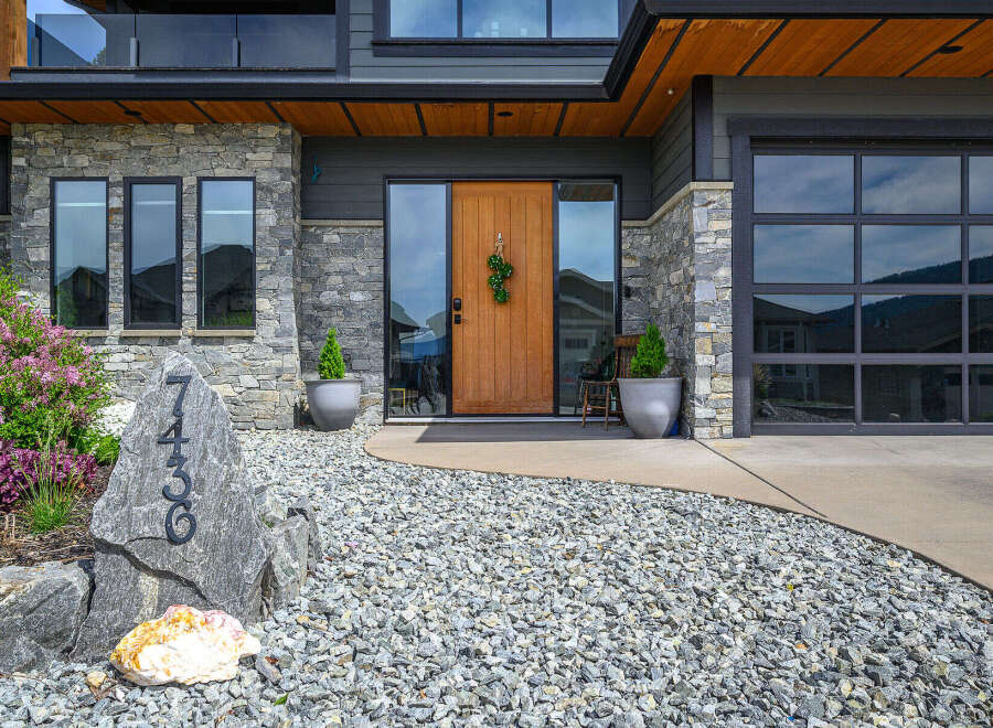 This stunning property boasts a modern facade with a beautiful stone exterior and a welcoming wooden door.